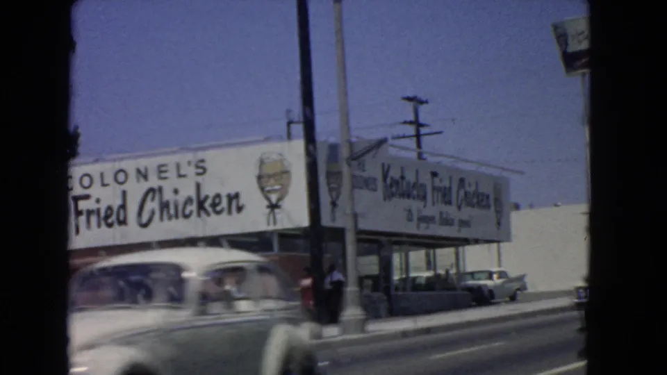 A fast-moving 1966 San Pedro street frame shows a blurred car crossing the Kentucky Fried Chicken exterior.