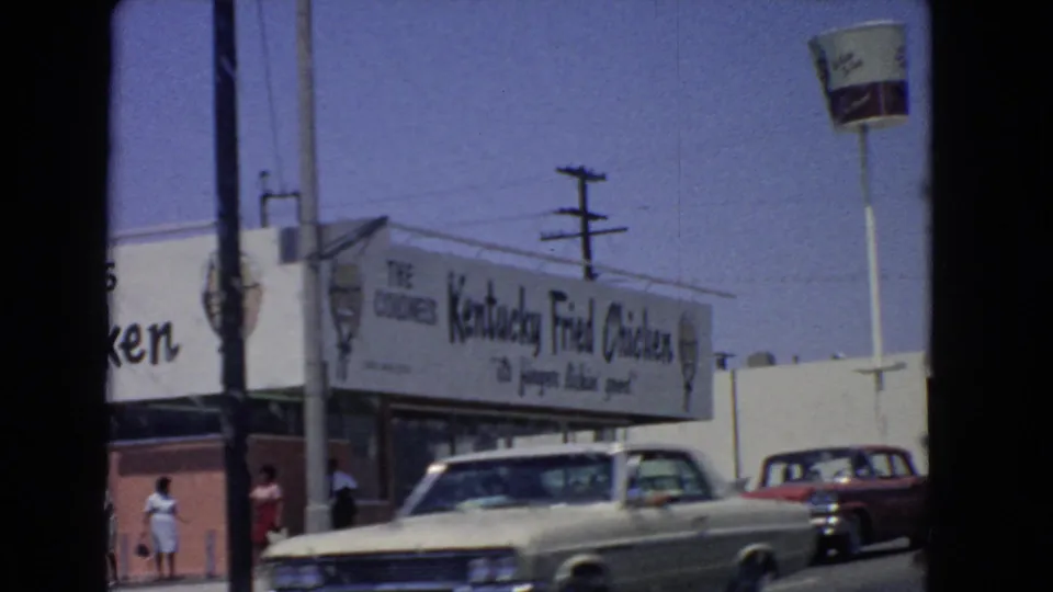 1966 San Pedro side view of a Kentucky Fried Chicken building, pedestrians, period cars, utility poles, and bucket sign.