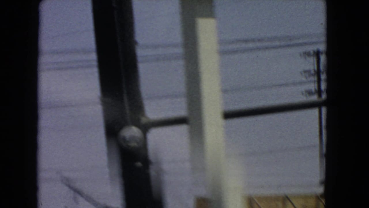 Blurred vehicle-window view with dark window frame, pale building wall, and overhead wires.
