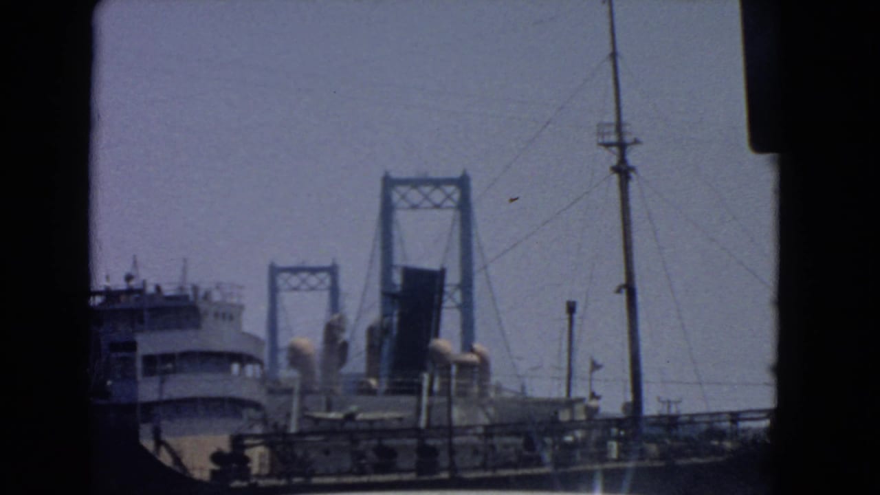 1966 San Pedro harbor view with a large ship in front of a raised drawbridge, seen through dark 8mm frame edges.