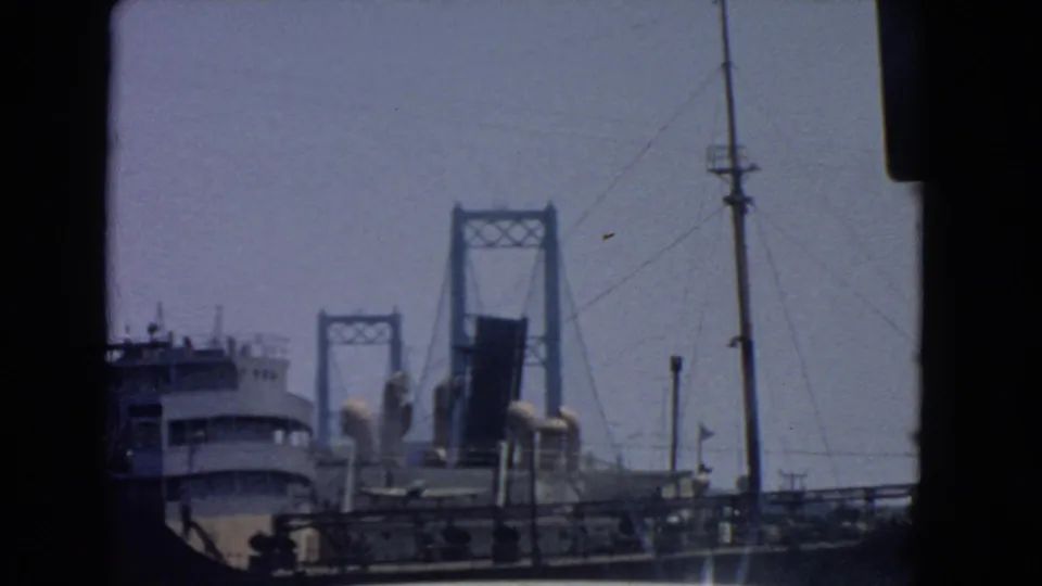 1966 San Pedro harbor view with a large ship in front of a raised drawbridge, seen through dark 8mm frame edges.