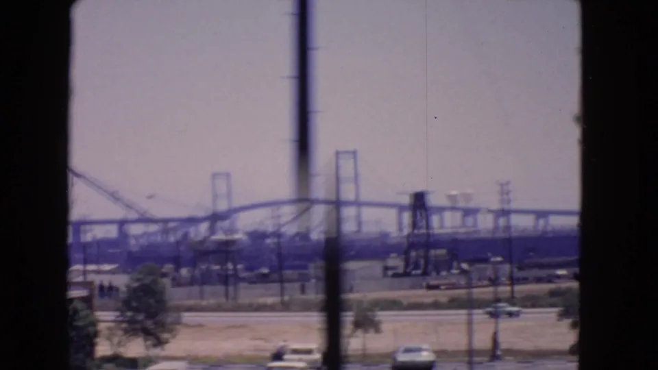 San Pedro industrial landscape in 1966 with a bridge under construction, cranes, utility lines, and cars passing below the frame.