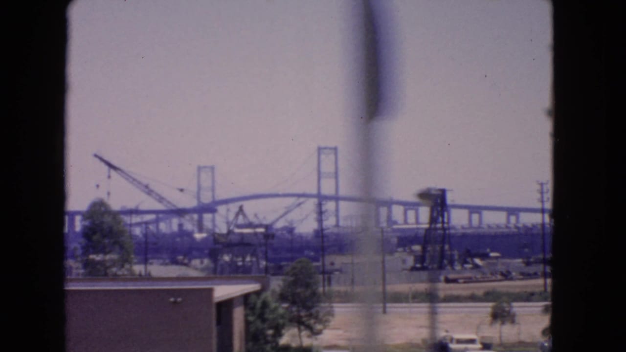 1966 San Pedro bridge construction view with cranes and industrial equipment, partly obscured by a soft window-frame blur.
