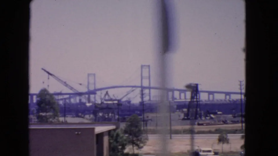 1966 San Pedro bridge construction view with cranes and industrial equipment, partly obscured by a soft window-frame blur.