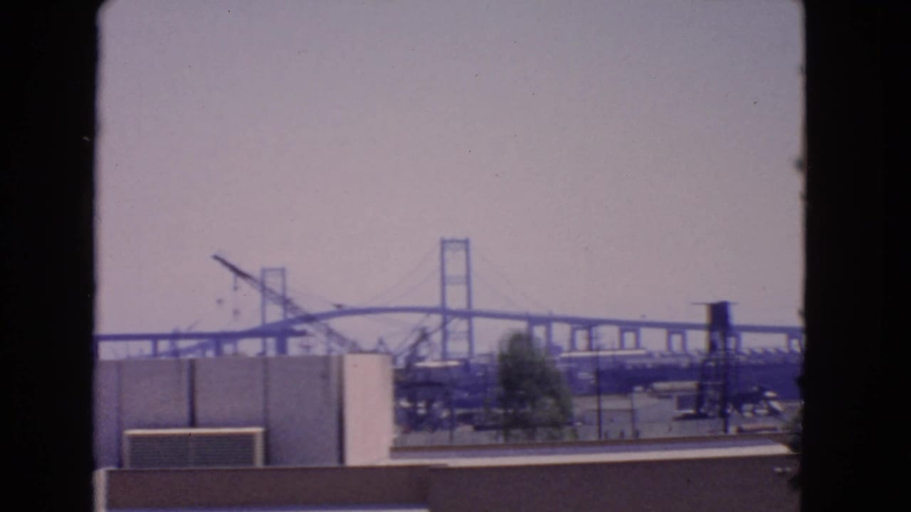 Distant suspension bridge and industrial waterfront seen from an elevated viewpoint.