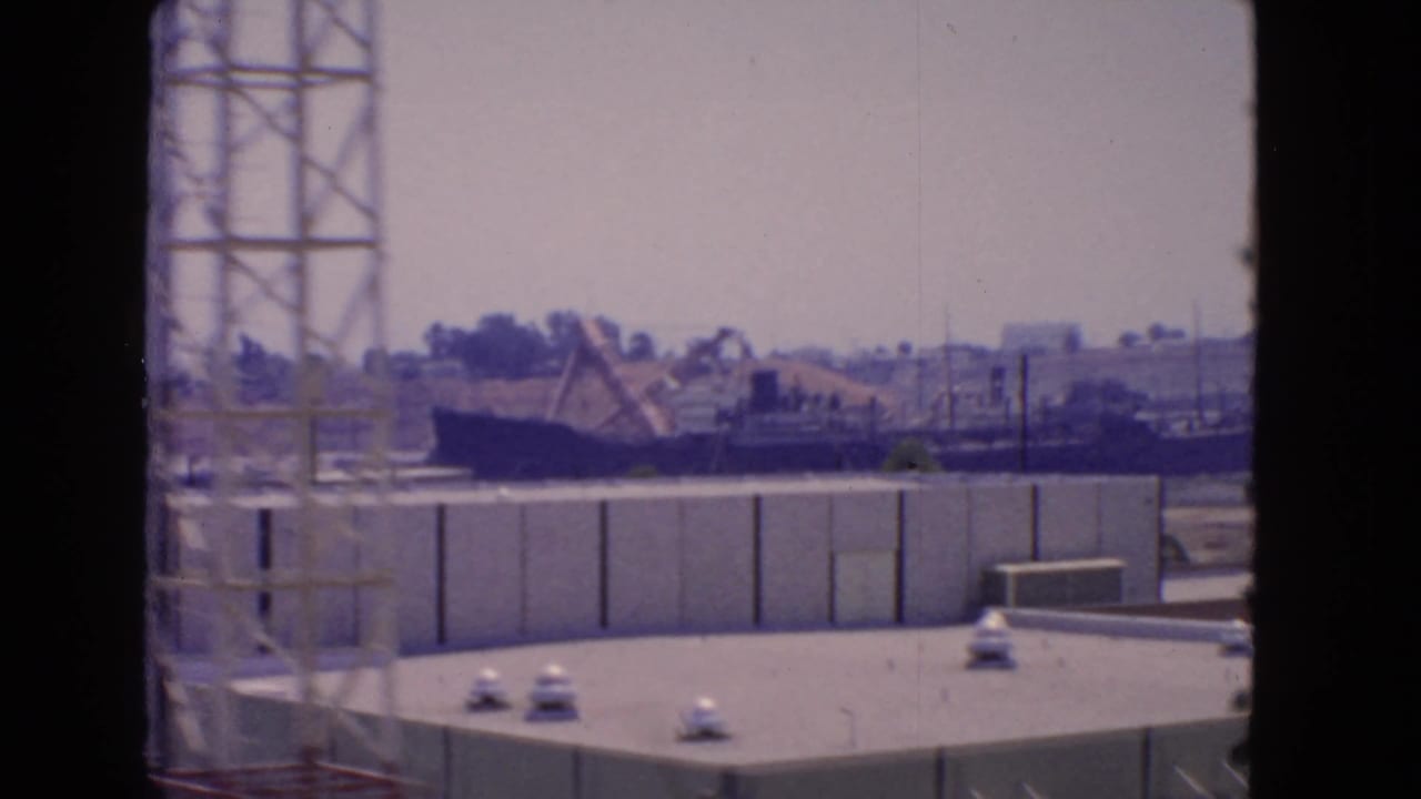 Industrial waterfront with rooftops, a tower structure, and equipment near the harbor.