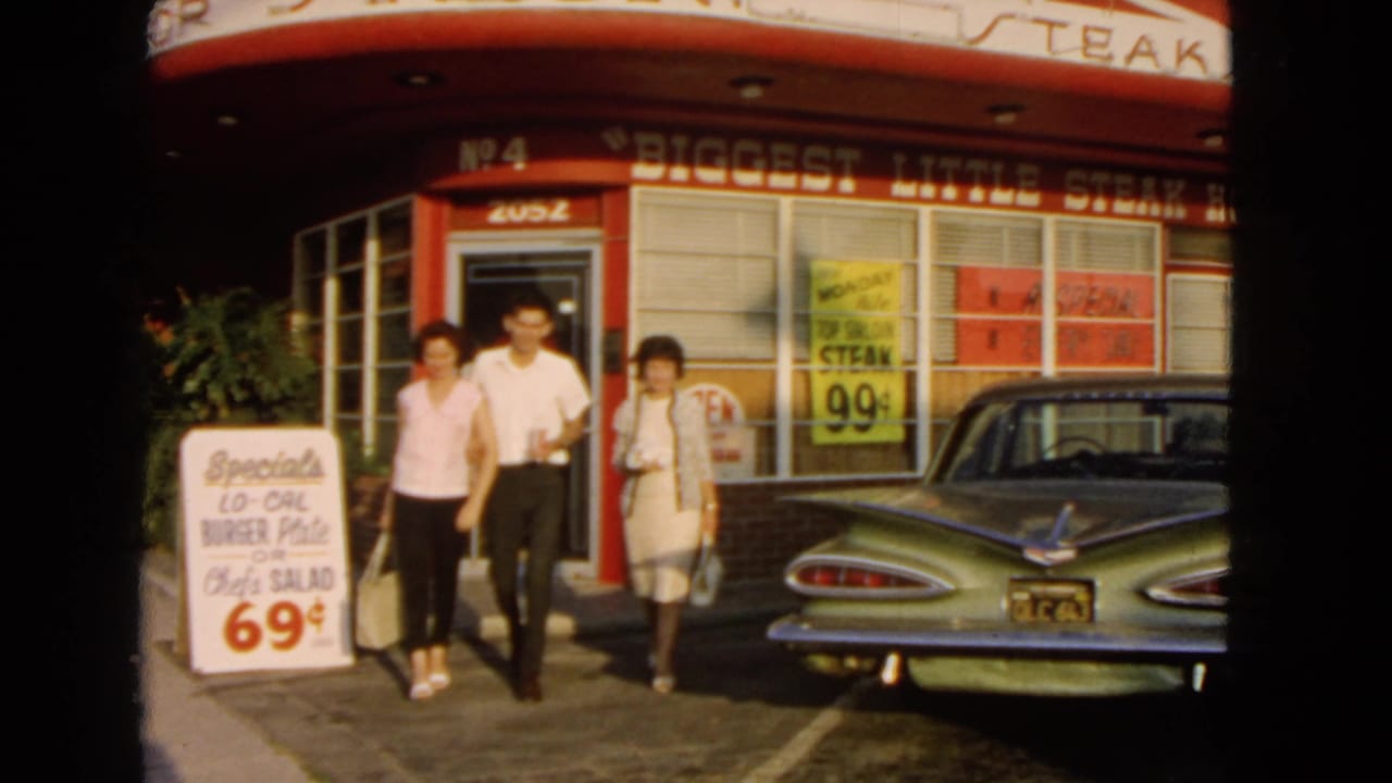 The group walks toward the camera outside the San Pedro steak house, with a green Chevrolet and price signs in the background.