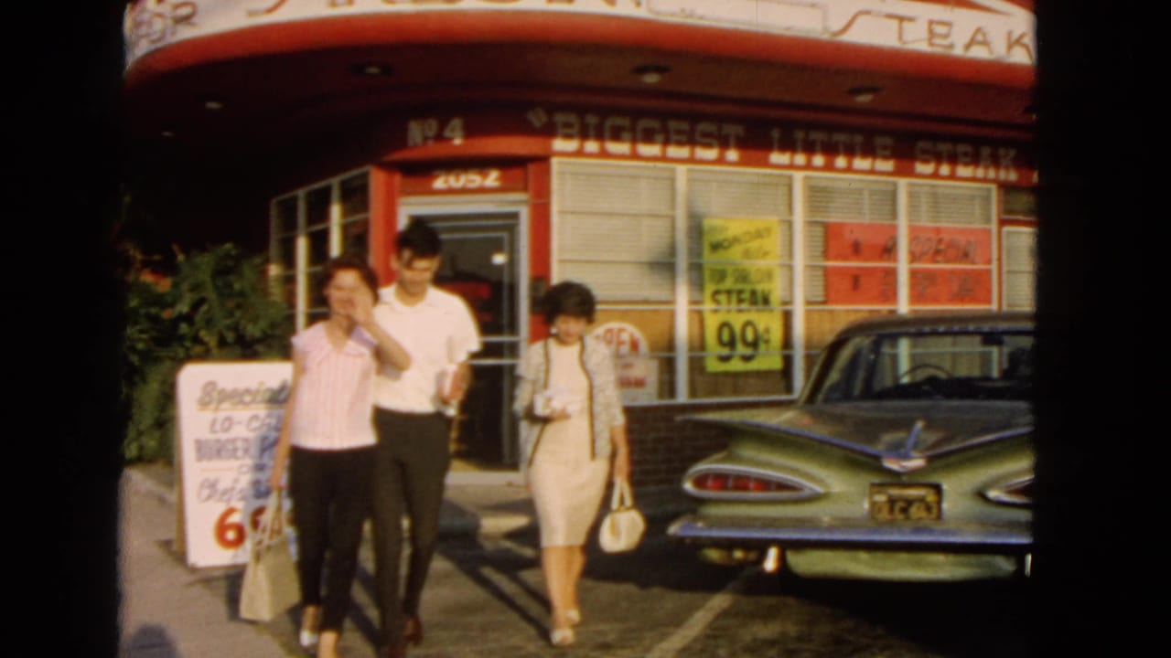 Outside the 1966 San Pedro restaurant, a young woman waves toward the camera as the group passes the sidewalk sign and car.