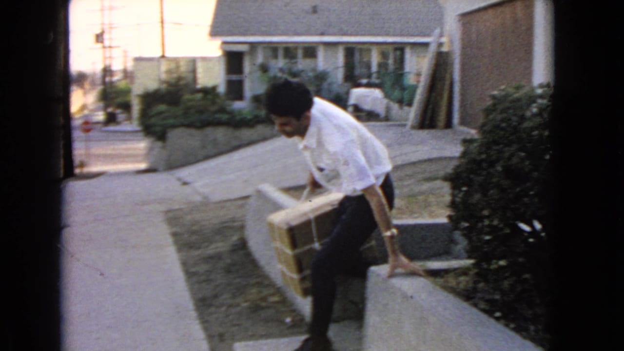 Man carries a large tied package down a sloped sidewalk near a house.
