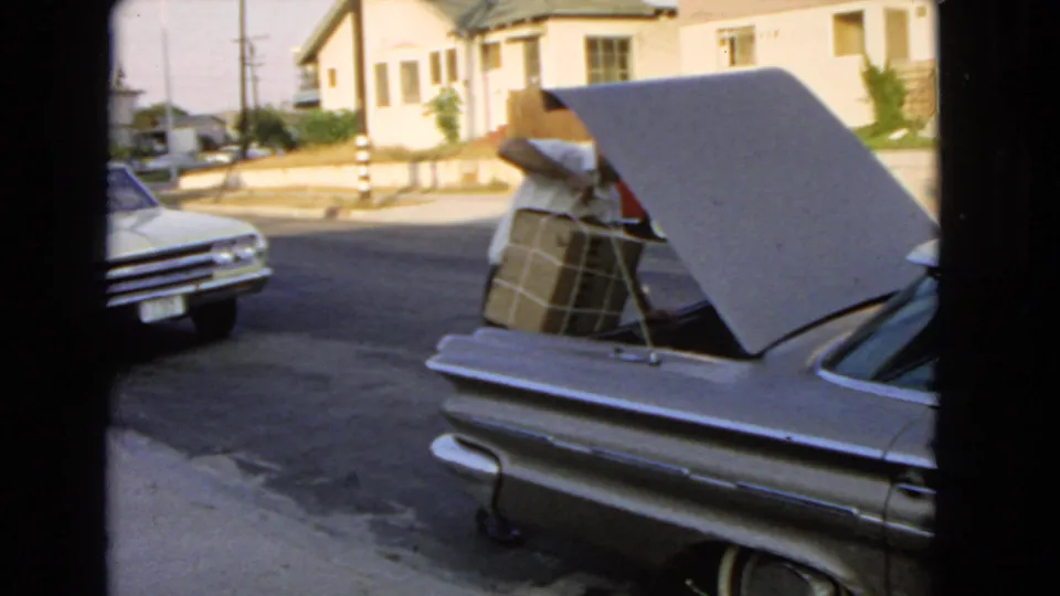 The large wrapped box is being pushed into the open trunk of a silver car on a suburban San Pedro street.