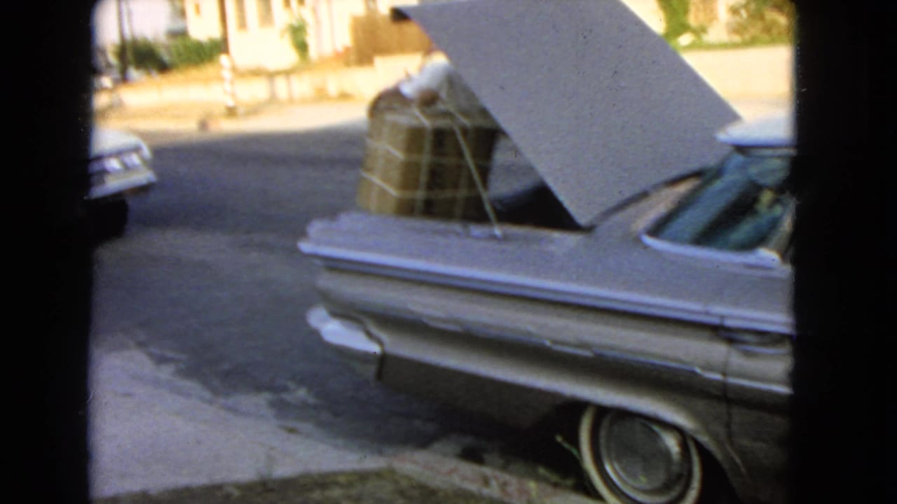 Silver sedan with open trunk loaded with boxes on a residential street.