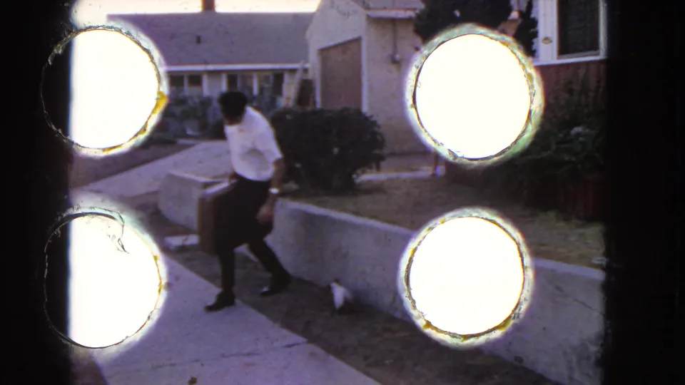 The man carries a suitcase toward the street outside a San Pedro house, with 8mm frame burn visible at the edge.