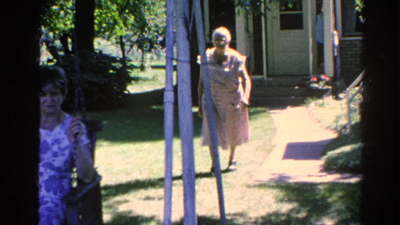 Two women are seen near a porch and garden path outside a house.