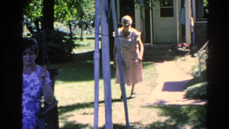 Two women appear outside a Silver Lake house, one seated near the porch and one walking along a sunny garden path.