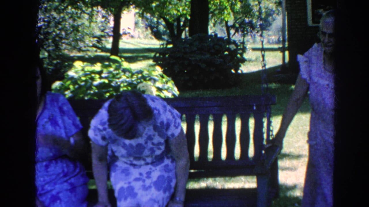 Women gathered around a wooden bench in a shaded garden.