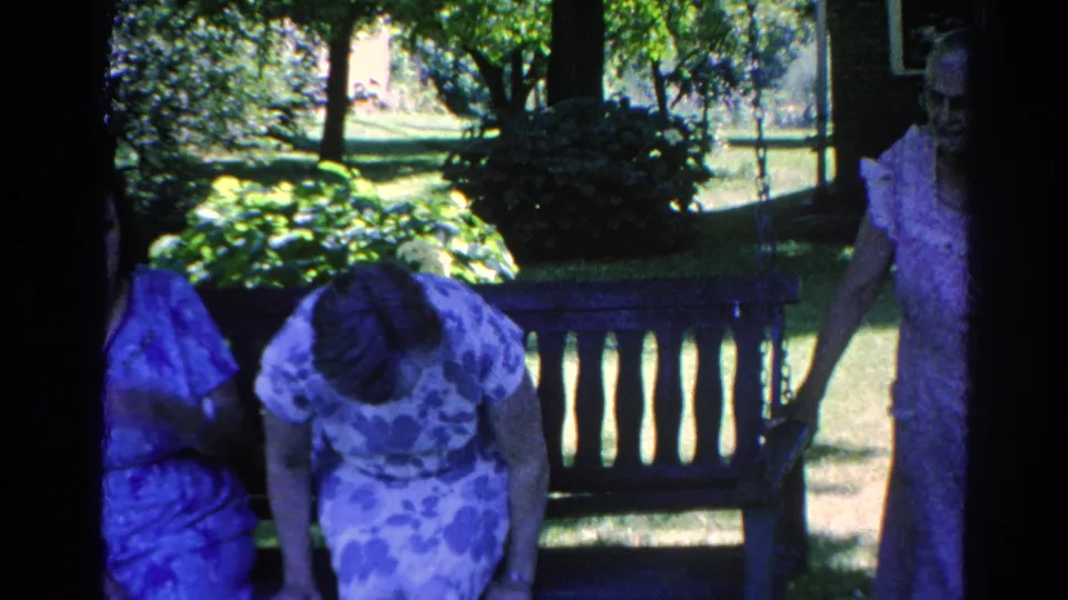 Adult women sit and stand around a wooden bench in a Silver Lake garden, with lawn and trees visible beyond them.