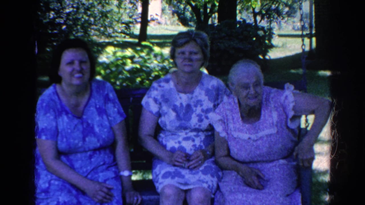 Three women in patterned summer dresses sit together on a bench in the 1966 Silver Lake home-movie scene.