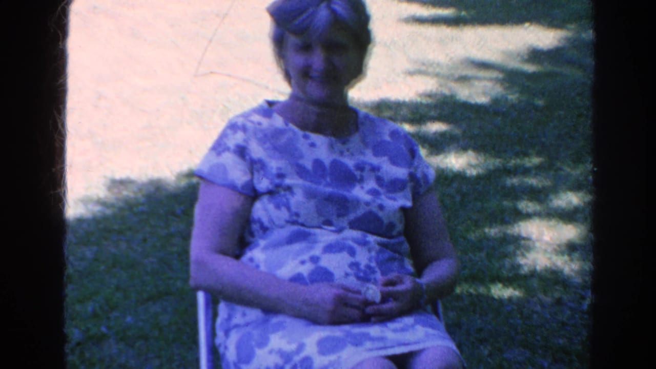 Woman seated outdoors in a folding chair with hands in her lap.