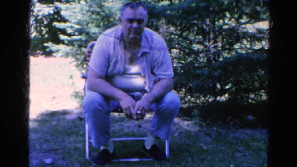 Adult man seated on a folding chair in a Silver Lake backyard, filmed on 8mm home-movie footage from 1966.
