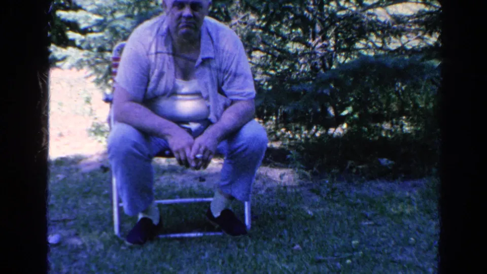 A man sits on a folding chair in a grassy Silver Lake yard, captured in softly colored 1966 8mm footage.