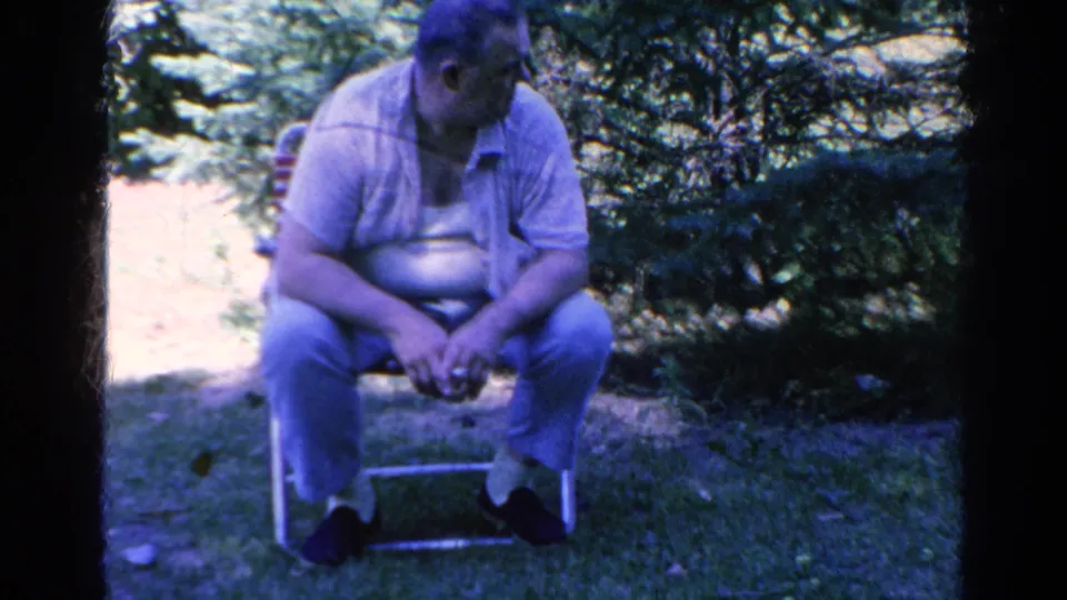 Adult man in a backyard chair looks down briefly in 1966 Silver Lake 8mm home-movie footage.