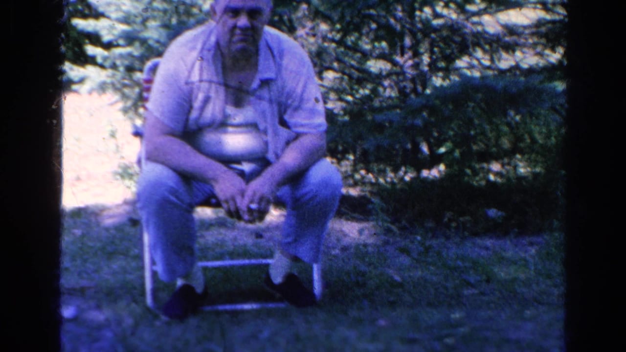 Man seated on a folding chair in a shaded grassy yard.