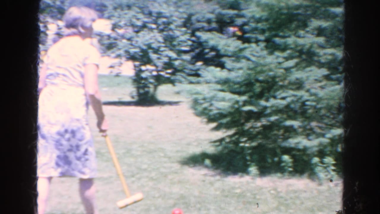 In 1966 Silver Lake home-movie footage, a woman in a light dress holds a croquet mallet on a sunny green lawn.