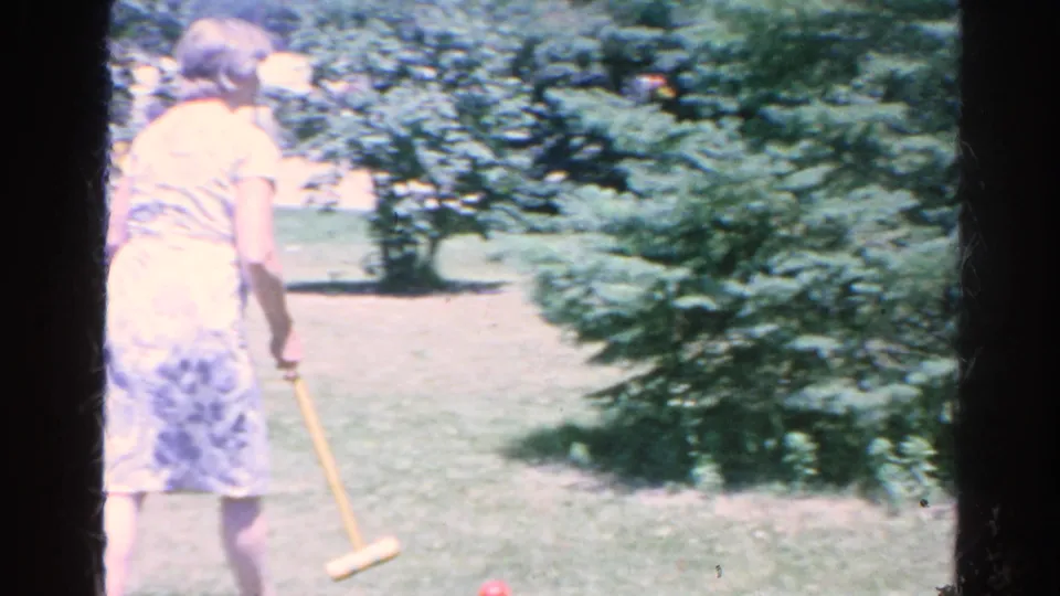 In 1966 Silver Lake home-movie footage, a woman in a light dress holds a croquet mallet on a sunny green lawn.