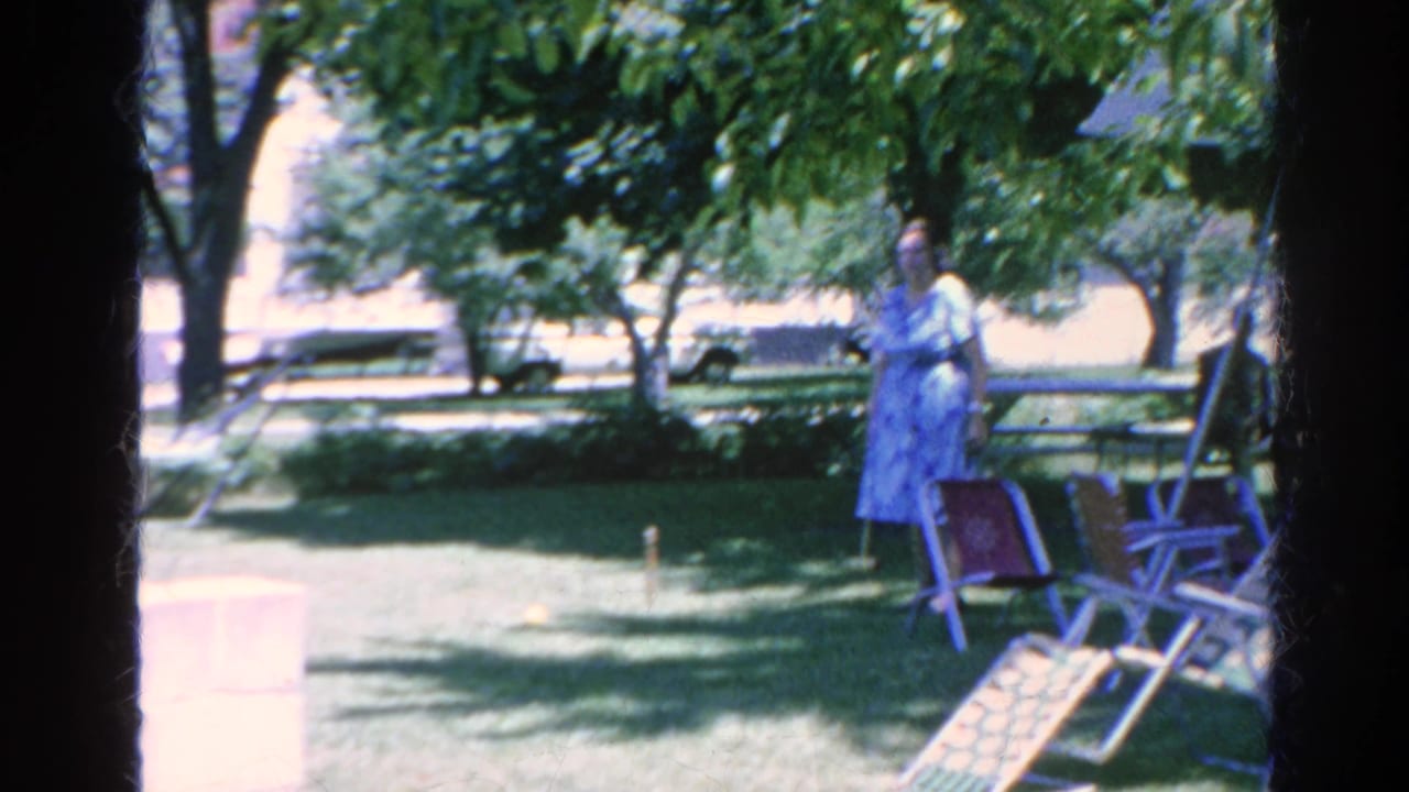 1966 Silver Lake home-movie frame showing two women in summer dresses near lawn chairs during a backyard croquet game.