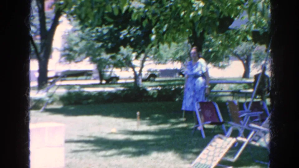 1966 Silver Lake home-movie frame showing two women in summer dresses near lawn chairs during a backyard croquet game.