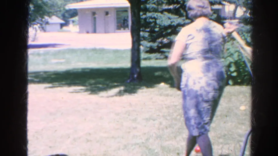In 1966 Silver Lake home-movie footage, a woman stands barefoot on a backyard lawn with a croquet mallet near a hammock and trees.