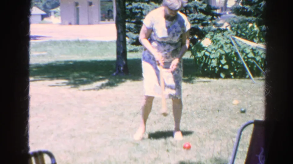 The 1966 8mm frame shows a woman bending over a croquet mallet, aiming toward a red ball in a Silver Lake backyard.
