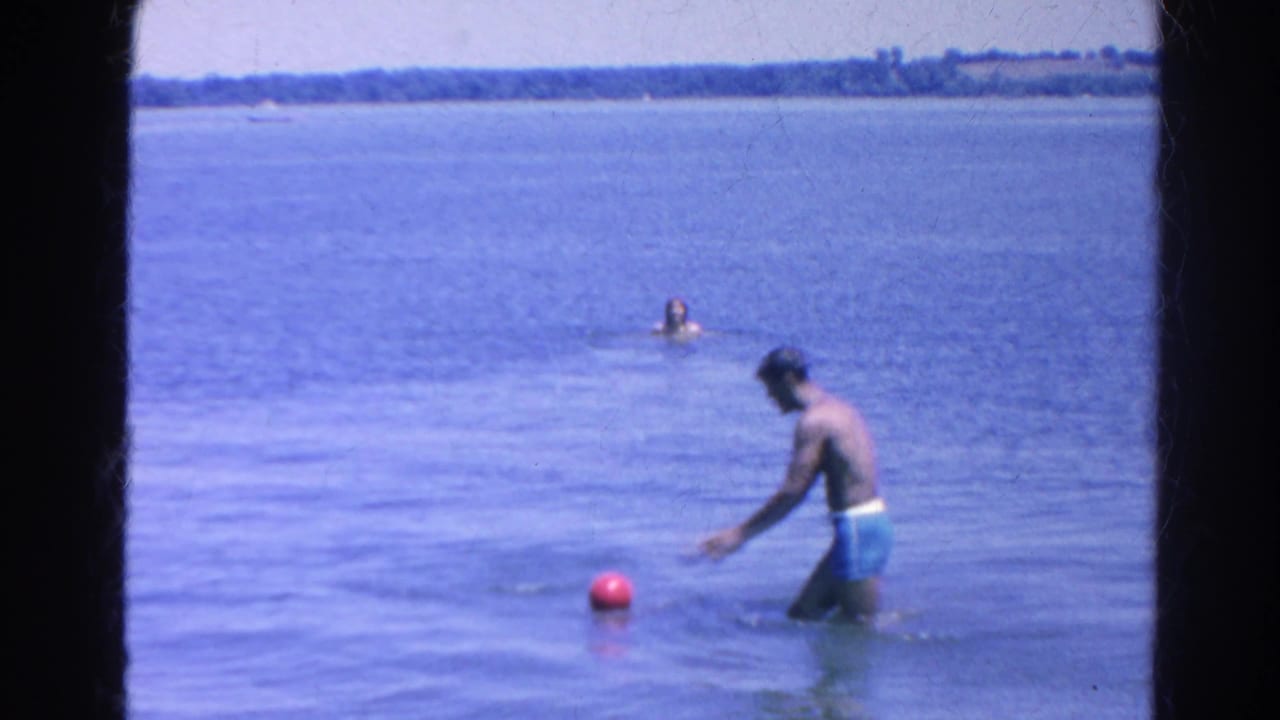 At Silver Lake in 1966, a man in blue swim trunks reaches for a red ball while others swim farther out.