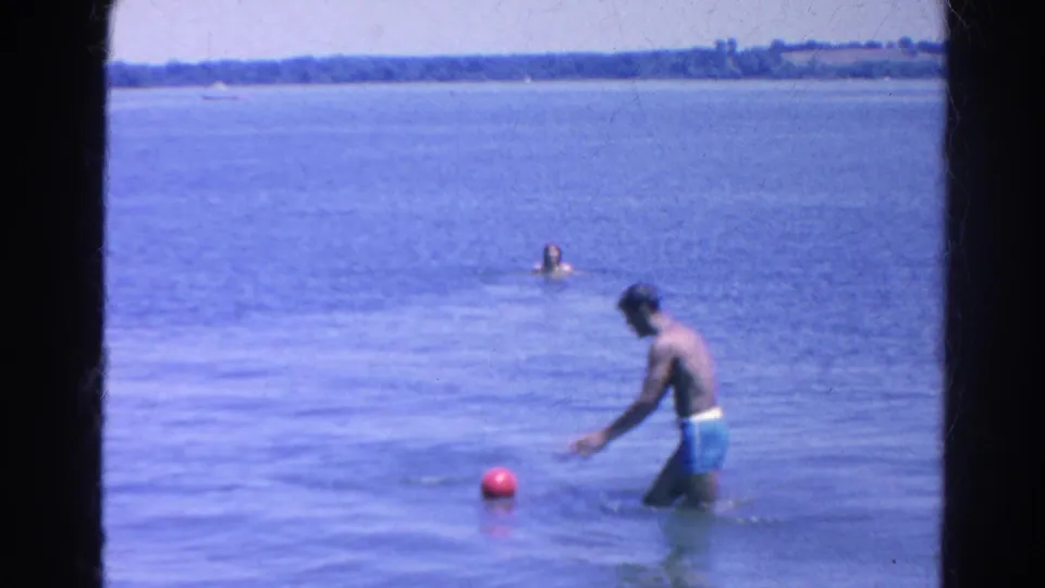 At Silver Lake in 1966, a man in blue swim trunks reaches for a red ball while others swim farther out.