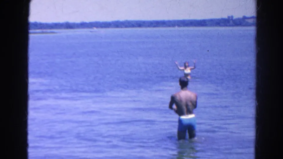 Home-movie frame from Silver Lake showing a man in shallow water facing another swimmer with raised arms.