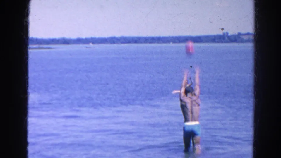 1966 Silver Lake frame showing a man lifting his arms as a red ball rises above him over the water.