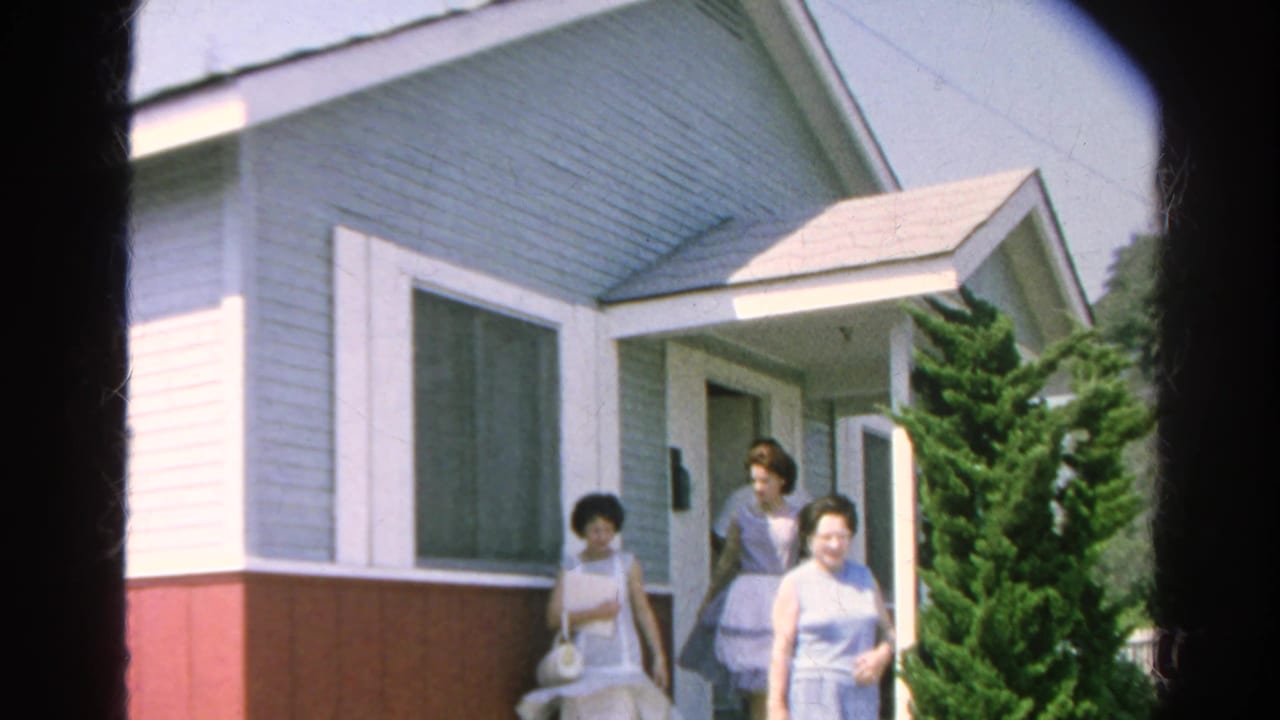 Three women walk away from the doorway of a small painted house.