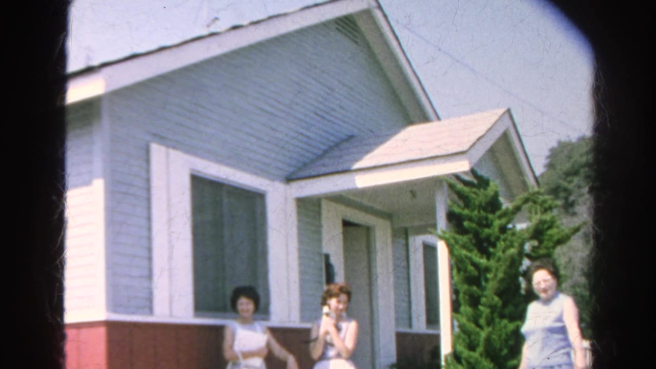 Three women stand near the porch as one woman moves at the right edge of the frame.