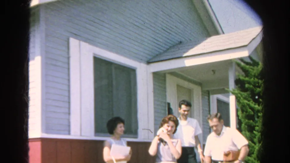 The 1966 home-movie frame shows adults outside a Silver Lake house, including a woman holding a cat beside the front entrance.