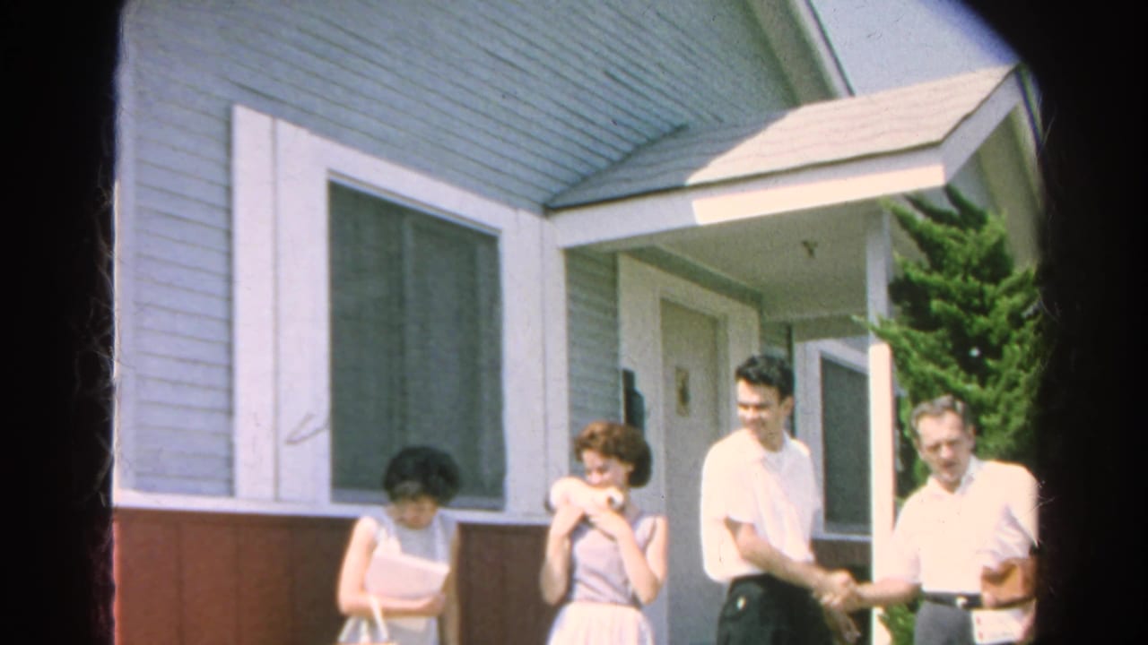 Adults in 1960s clothing stand outside a Silver Lake house, with two men shaking hands near the porch and two women nearby.