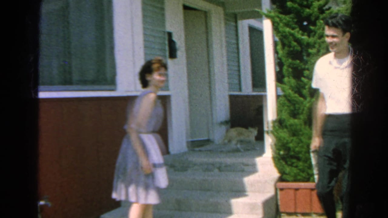 A woman moves near the porch doorway while a man in a white shirt stands nearby and a cat walks close to the entrance in Silver Lake.