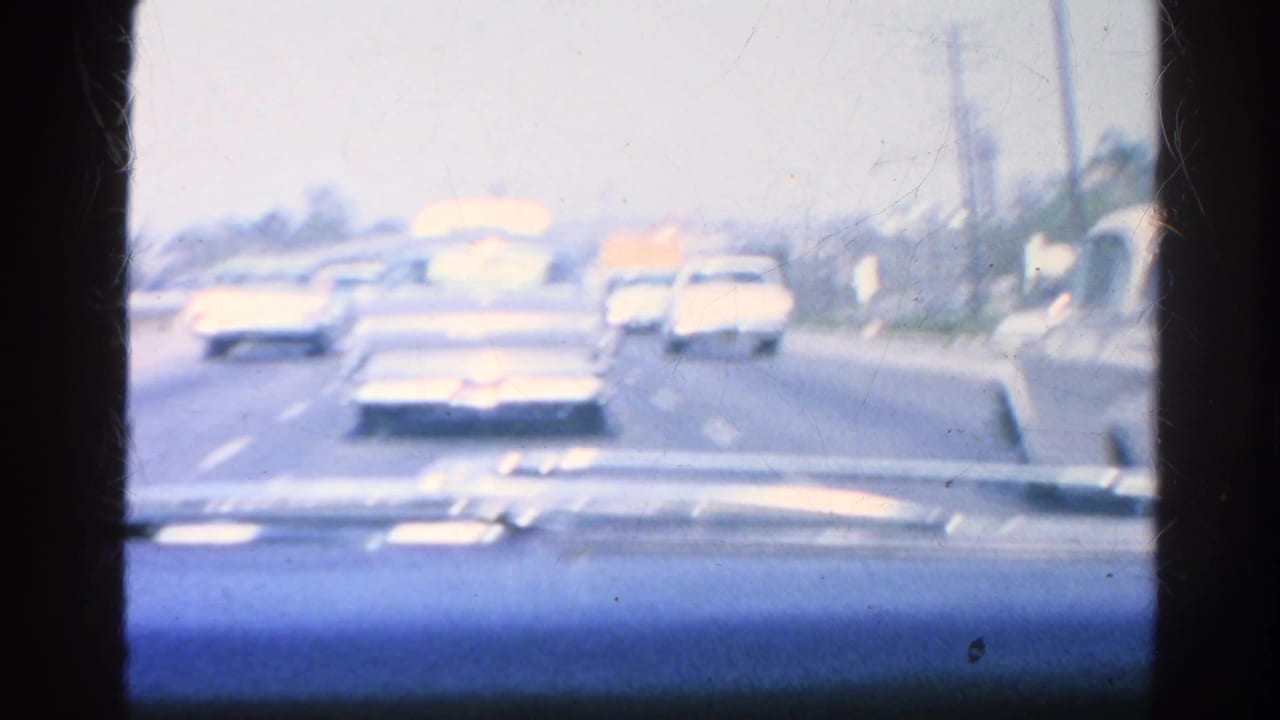 Cars travel ahead on a broad roadway seen from inside a vehicle.