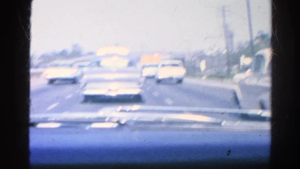 In-car 8mm view of 1960s automobiles moving along a broad road in Silver Lake, California, with the blue-tinted dashboard across the lower frame.