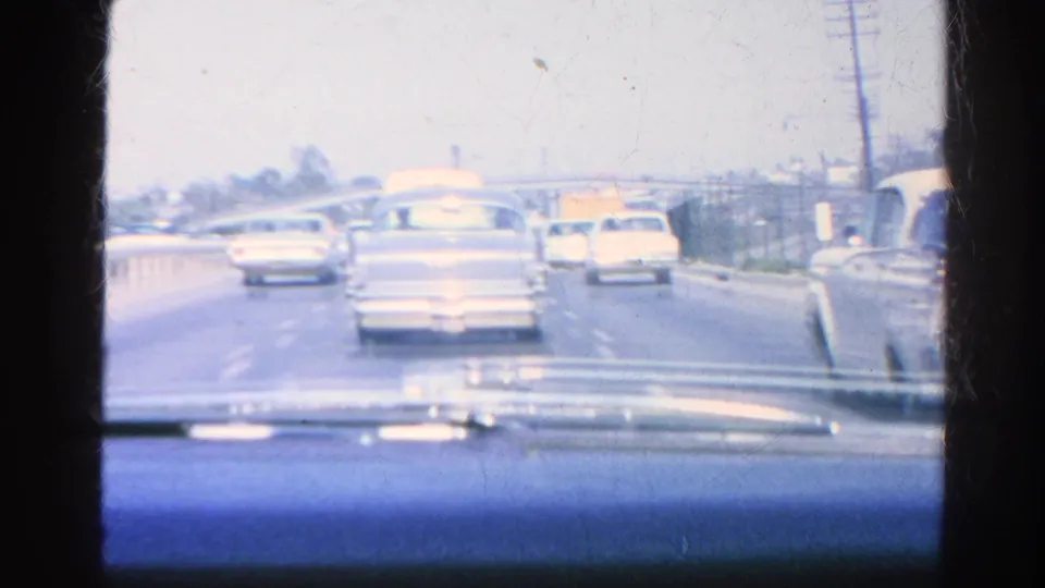 Passenger-perspective 1966 home-movie frame showing sedans and a station wagon in slow traffic on a multi-lane Silver Lake roadway.