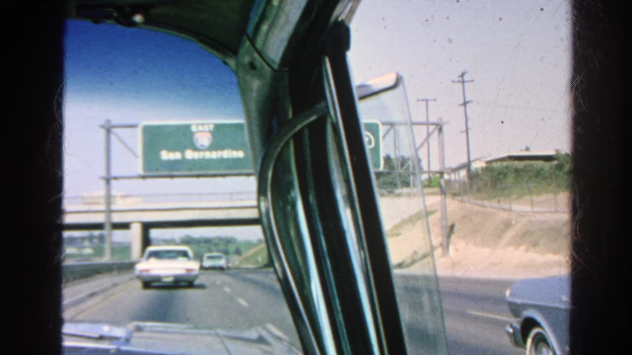 Freeway view from inside a car with an overhead San Bernardino sign and 1960s traffic.