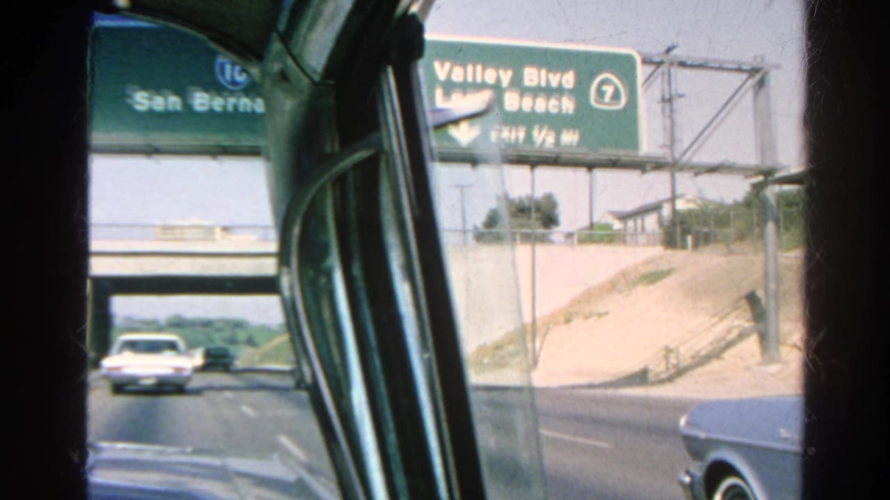 Freeway approach with overhead signs for San Bernardino and Valley Blvd visible through a car window.