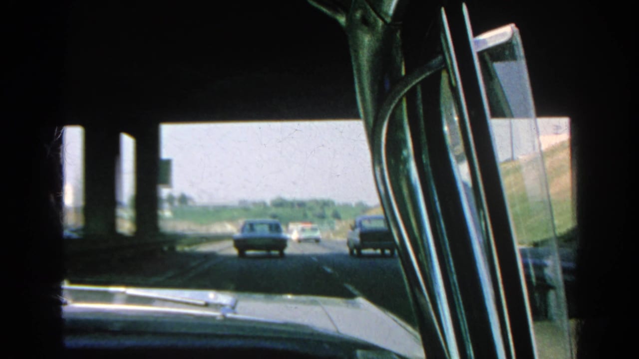 Freeway traffic seen through a car windshield and side window under an overpass.