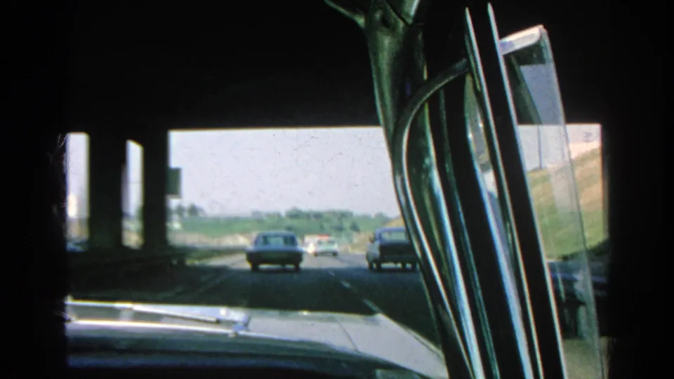 1966 Southern California freeway traffic viewed from inside a vintage car, with other vehicles ahead and dark overpass shadow above.