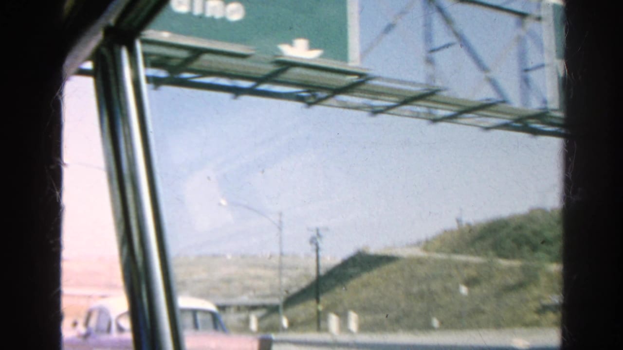 Car-window view of a highway sign and roadside hills from a moving vehicle.