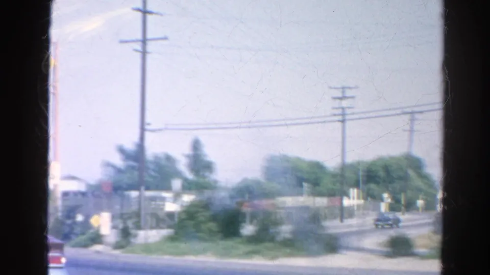 Moving 8mm car-window view in Southern California, with utility poles, small roadside buildings, traffic, and soft motion blur.